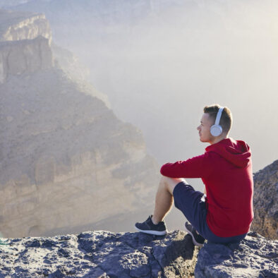 Person sitting on the edge of a ravine listening to a climbing podcast