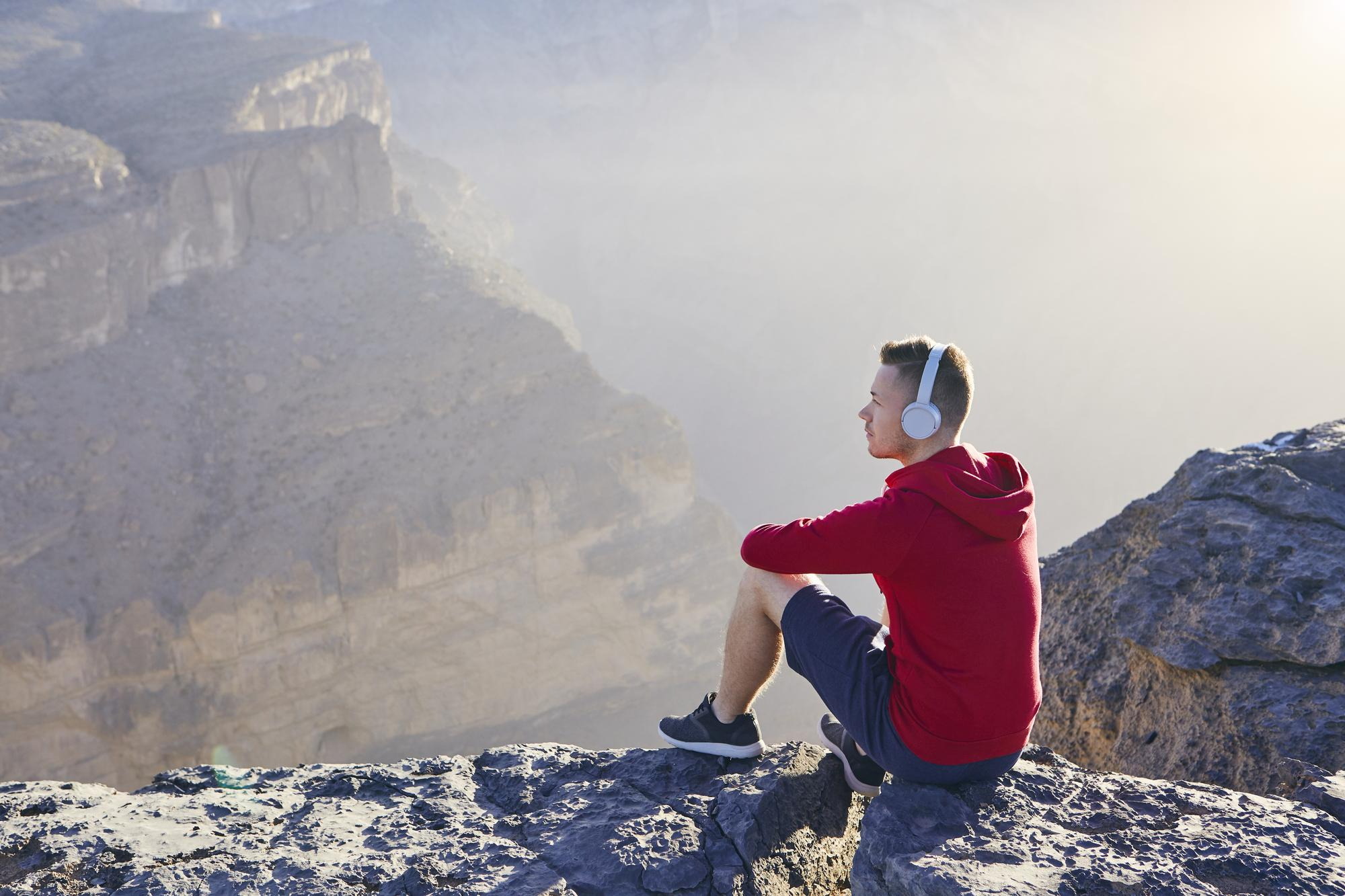 Person sitting on the edge of a ravine listening to a climbing podcast